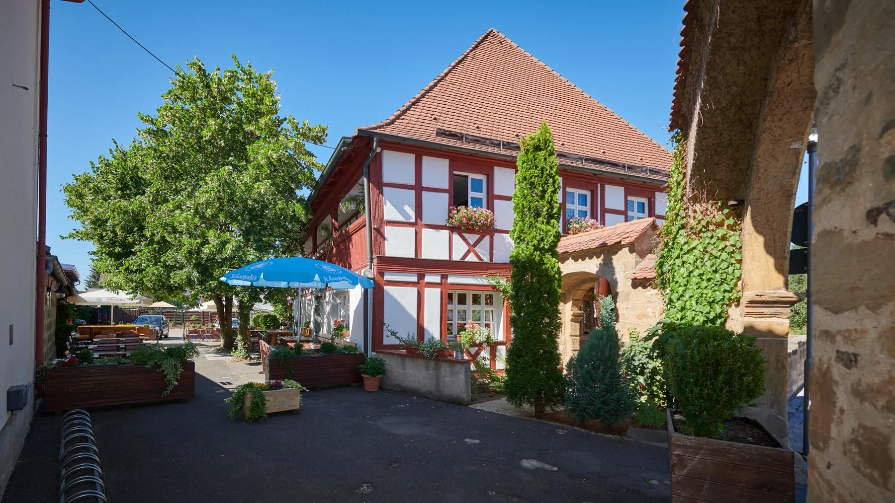 Der Biergarten im Innenhof des Egloffsteiner Hofs mit Tischen, Sonnenschirmen und großem Laubbaum vor dem Fachwerkhaus