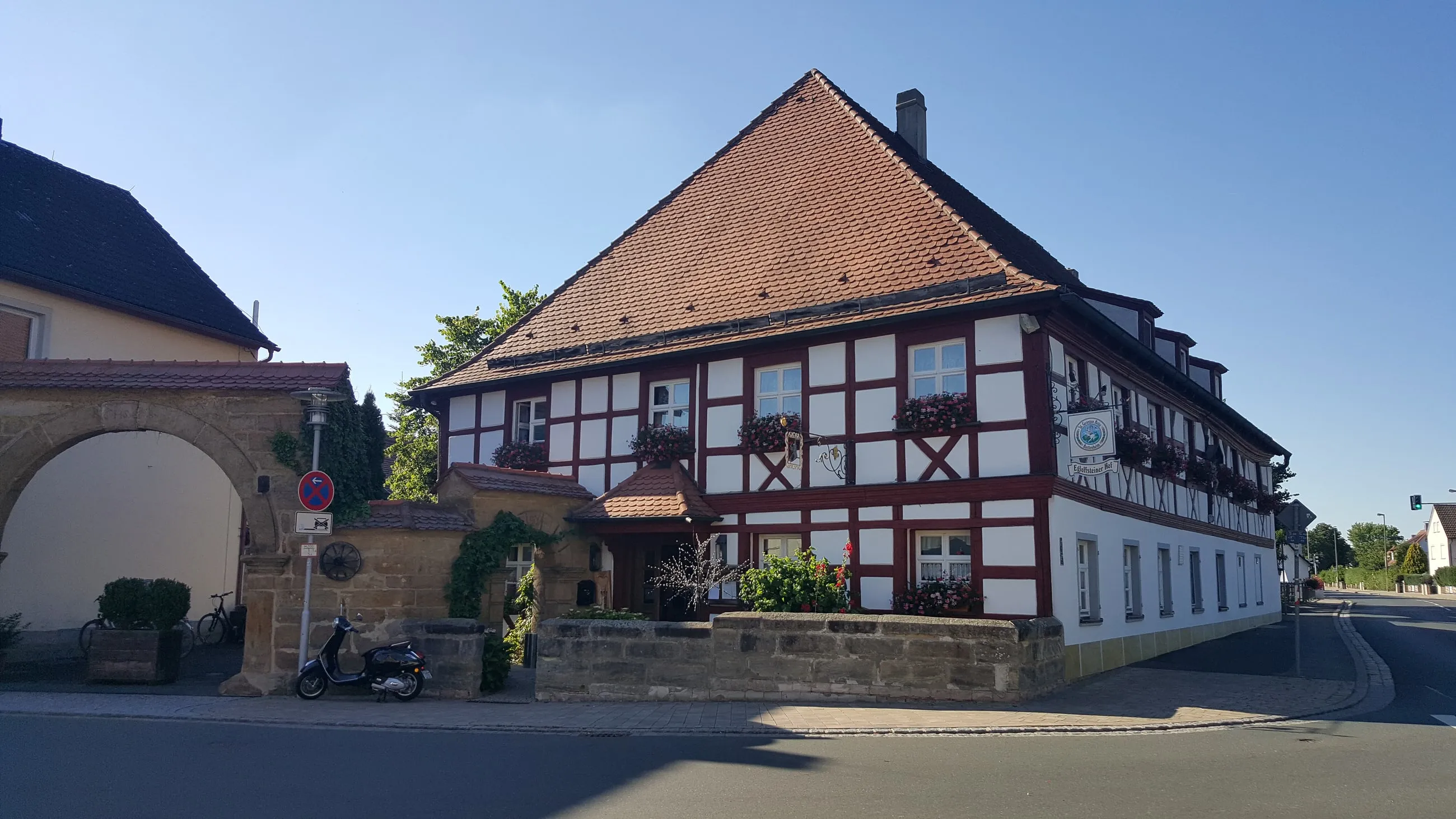 Der Egloffsteiner Hof in Altendorf: rot-weißes Fachwerkhaus mit Ziegeldach und blühenden Blumenkästen, daneben der alte Sandsteintorbogen