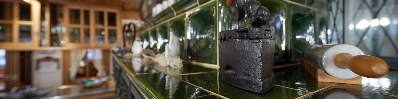 Detailaufnahme der grünen Ofenkacheln mit historischem Bügeleisen und Nudelholz