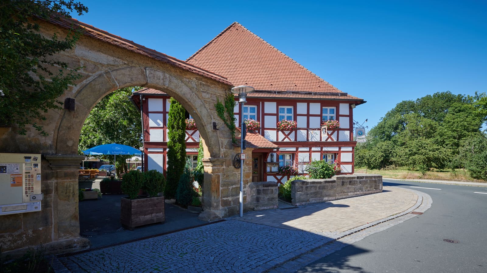 Sandsteiner Torbogen des Egloffsteiner Hofs mit Blick in den Biergarten, dahinter das rot-weiße Fachwerkhaus